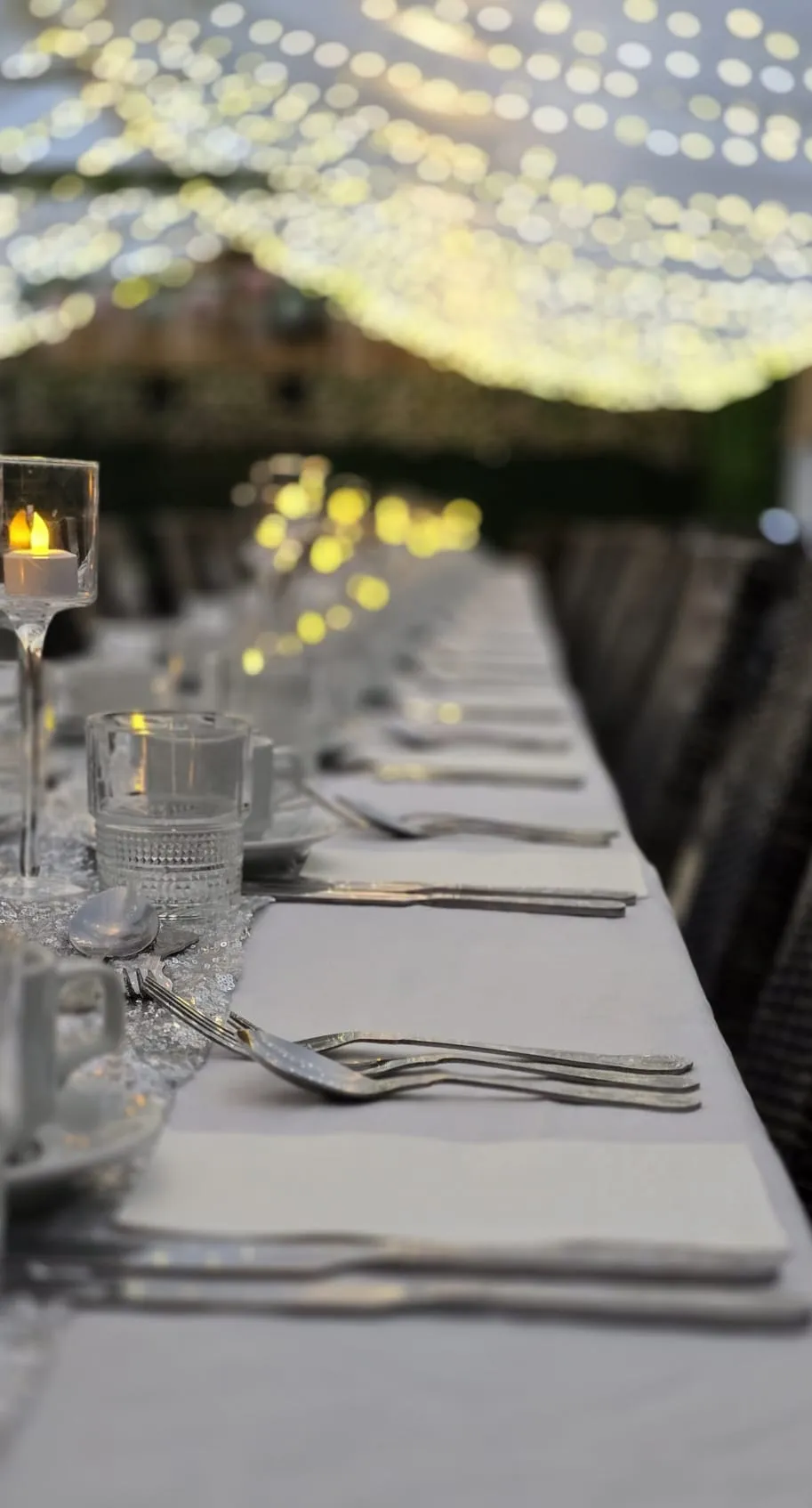 Tea lights and glassware along a dressed table after dark