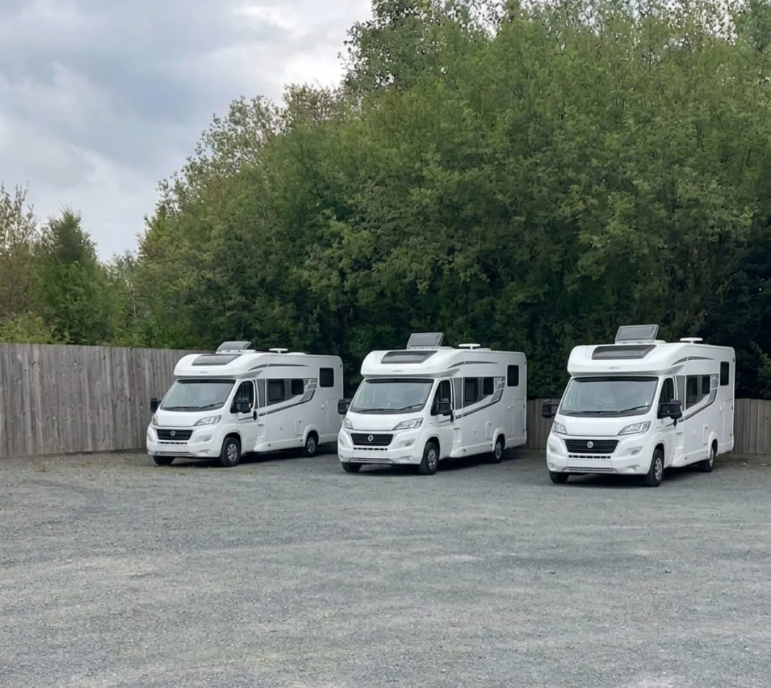 Three motorhomes parked side by side on the gravel car park at the Bryn Arms, a close-board fence and trees behind