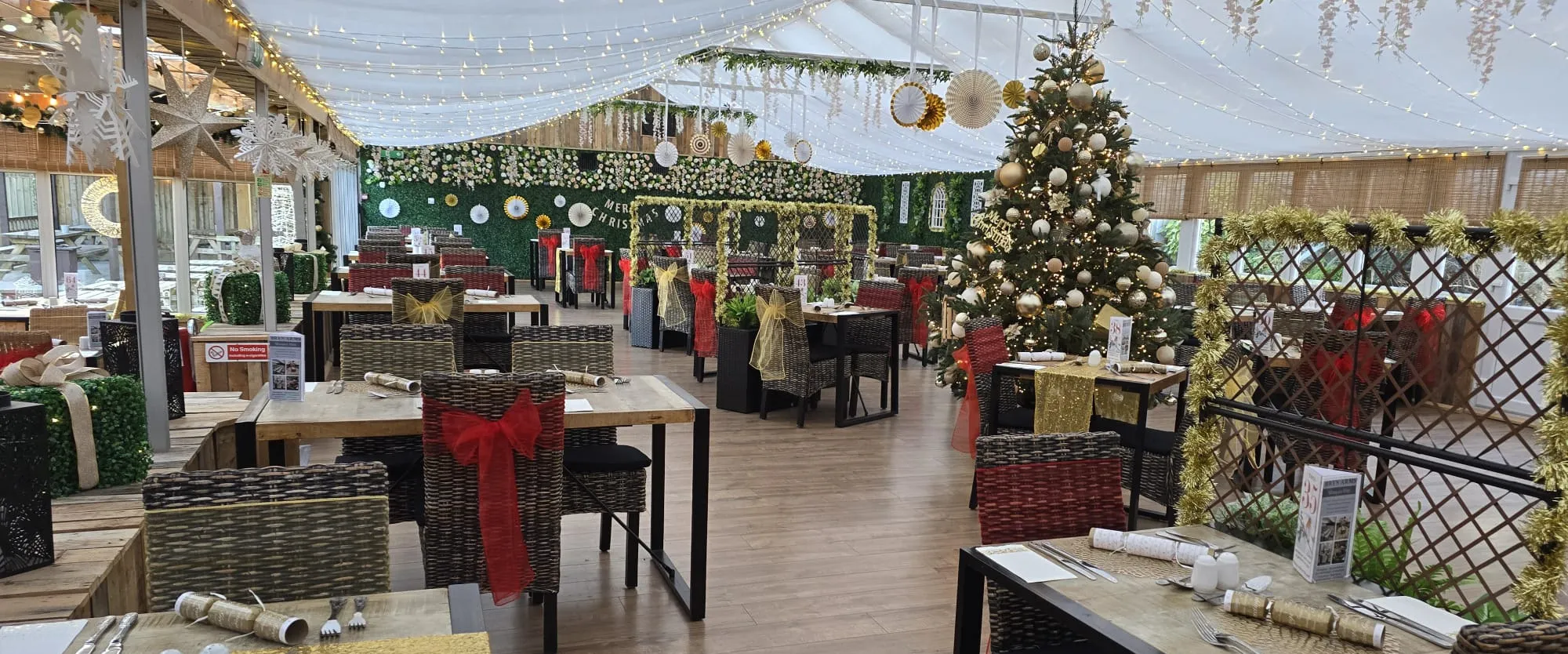 Across the laid Christmas tables toward the tree, trellis and foliage wall to the side