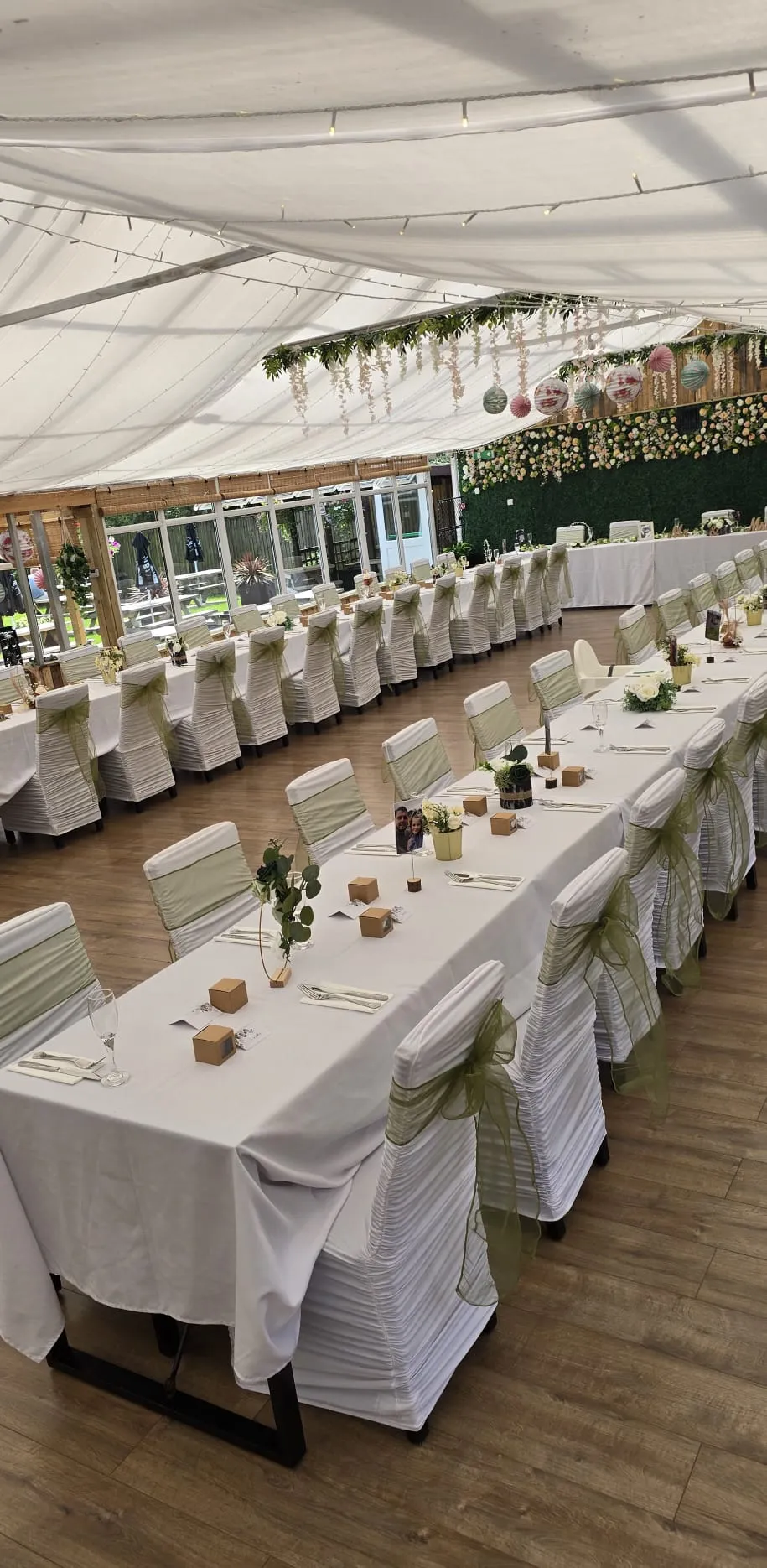 Long tables under the marquee with white covers, hessian sashes and green garlands