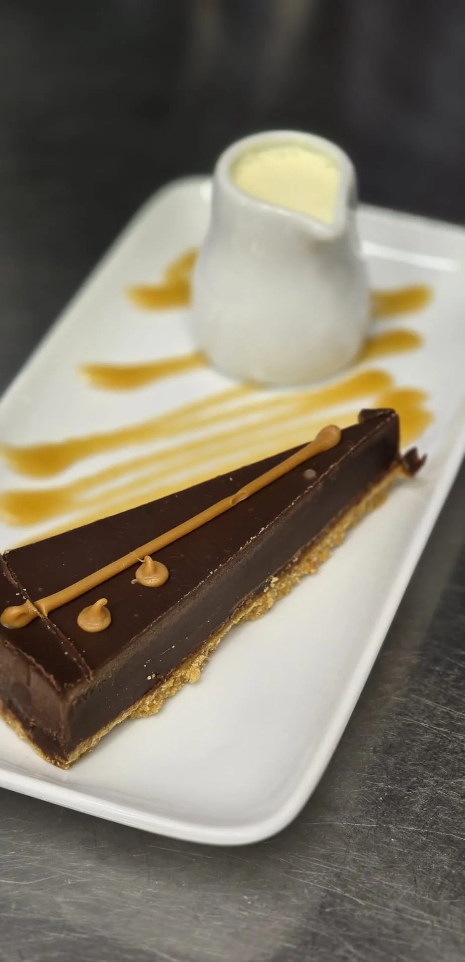 A slice of chocolate caramel tart with a jug of cream