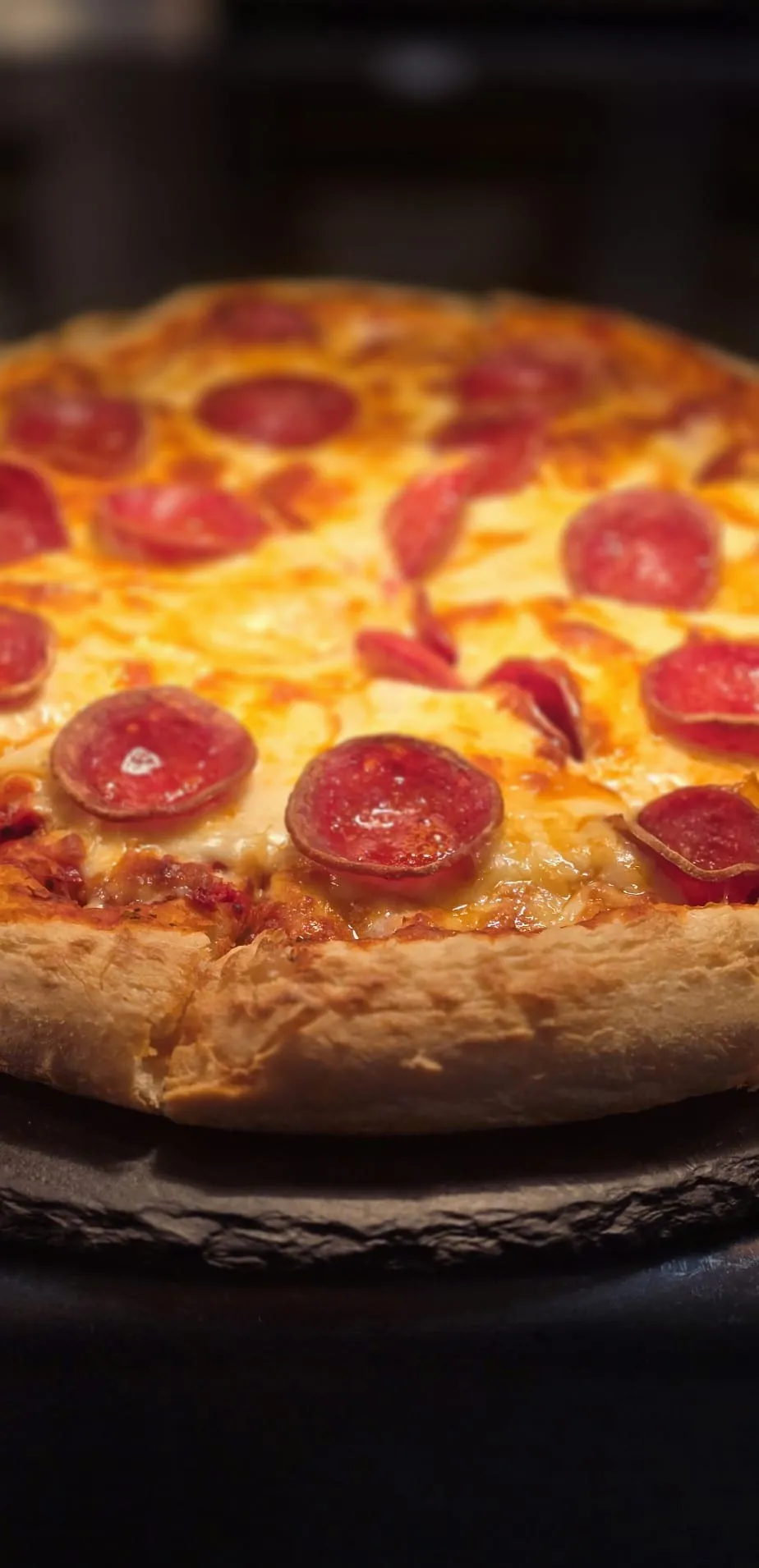 A whole pepperoni pizza with a golden crust on a slate board