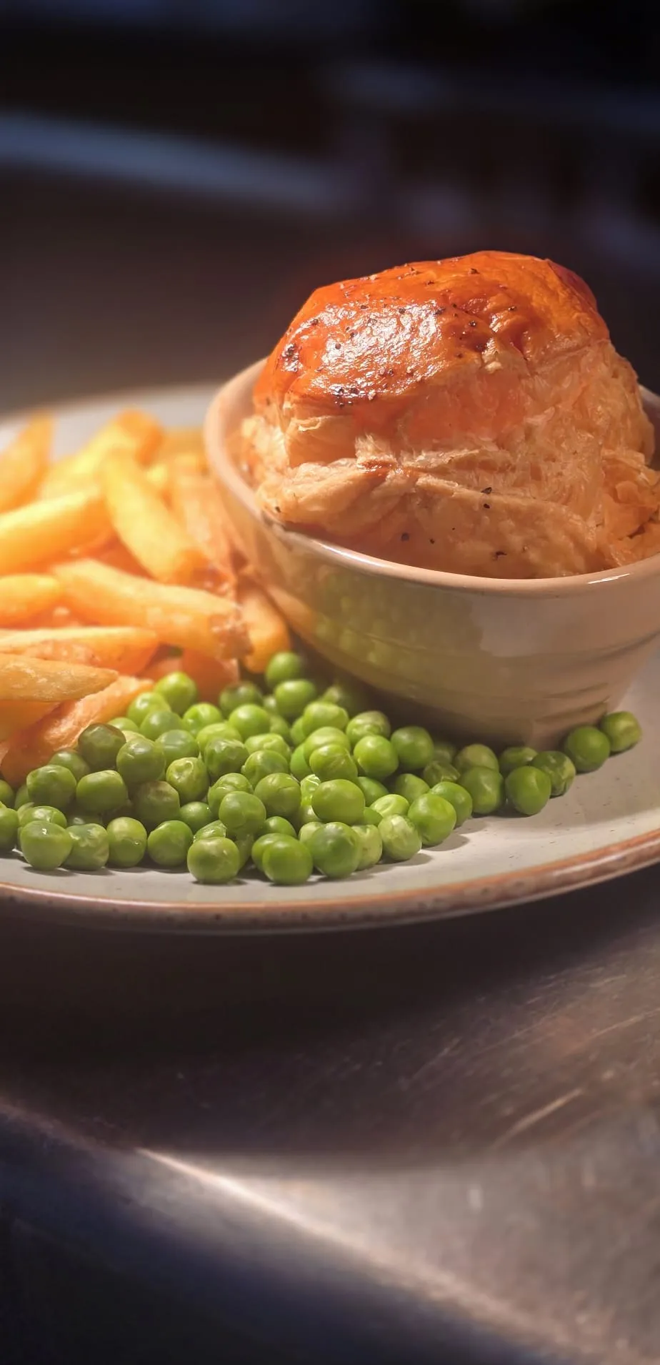 A golden puff pastry pot pie with chips and garden peas