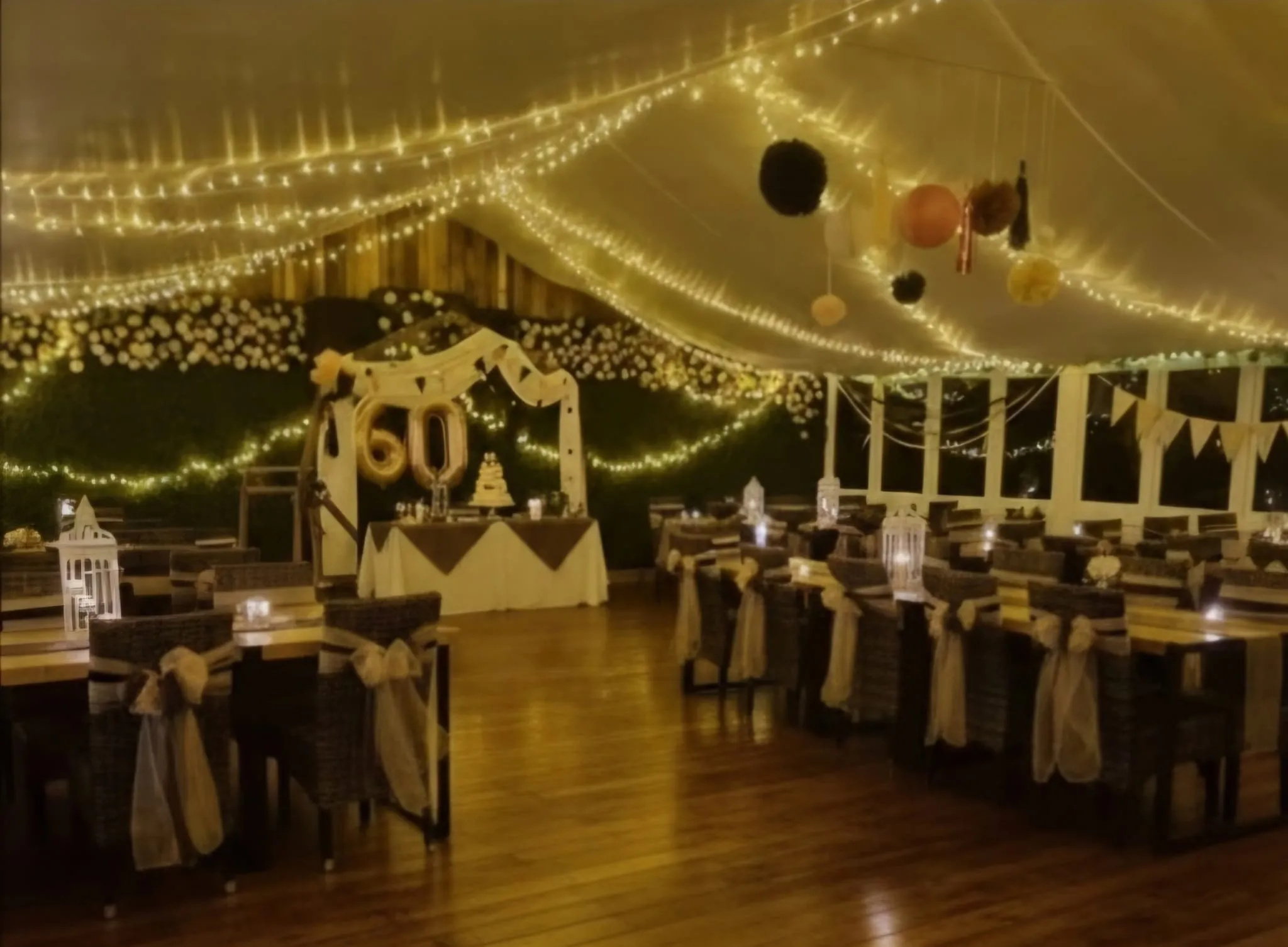 A 60th birthday party set up under fairy lights, with hessian sashes and a decorated backdrop