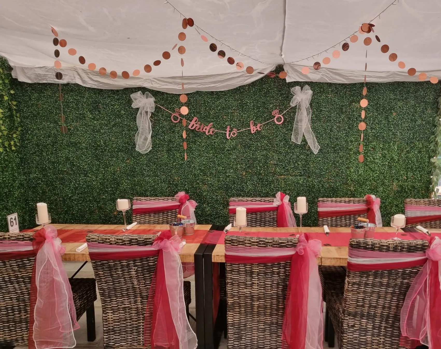 A hen party corner with a bride to be banner, rose gold garlands and a foliage wall