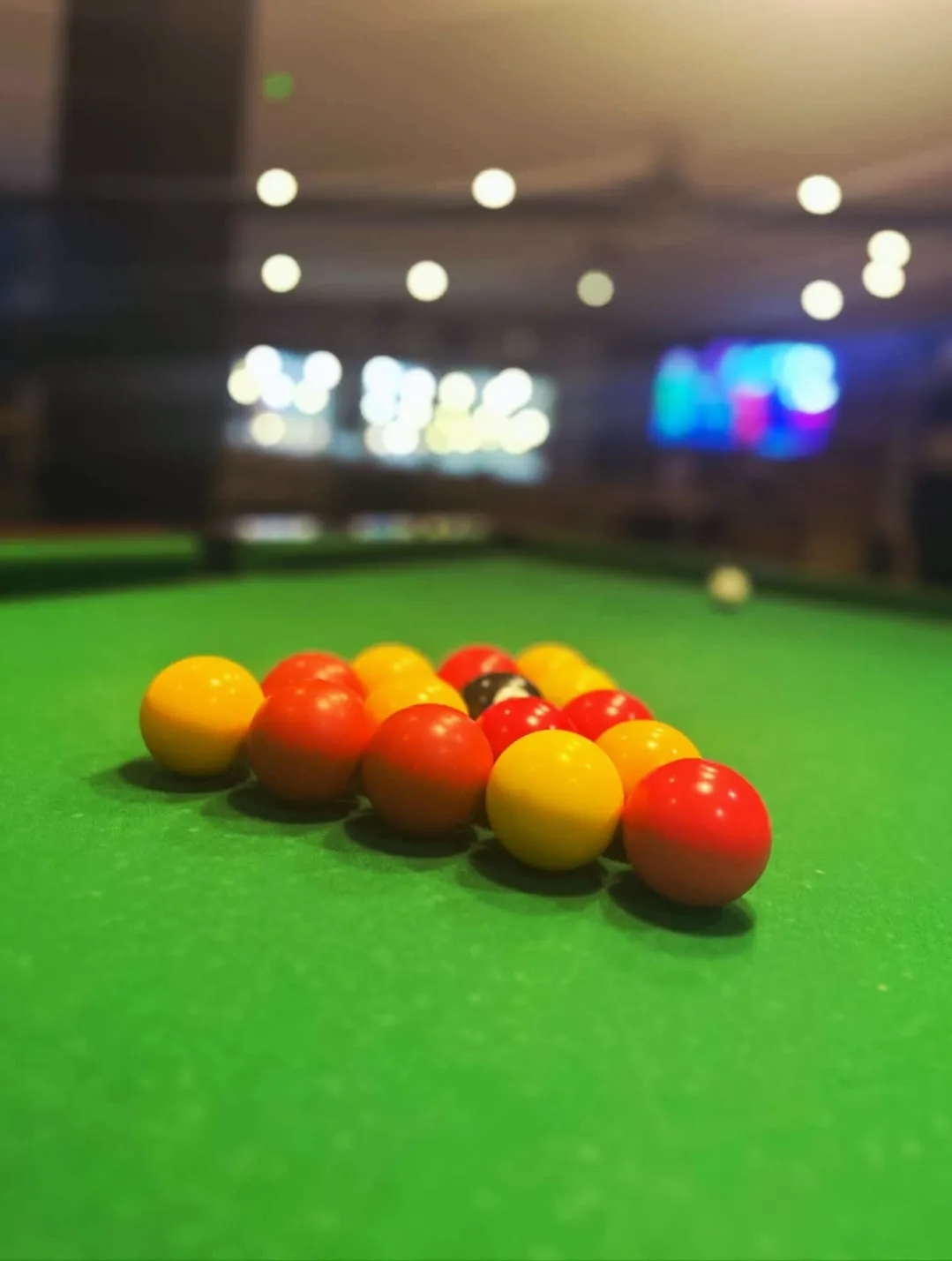 Racked reds and yellows on the pool table, the lights of the bar blurred behind