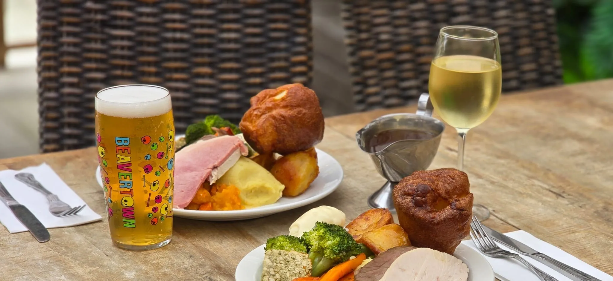 Two Sunday roasts with Yorkshire puddings and a gravy boat on a table in the beer garden