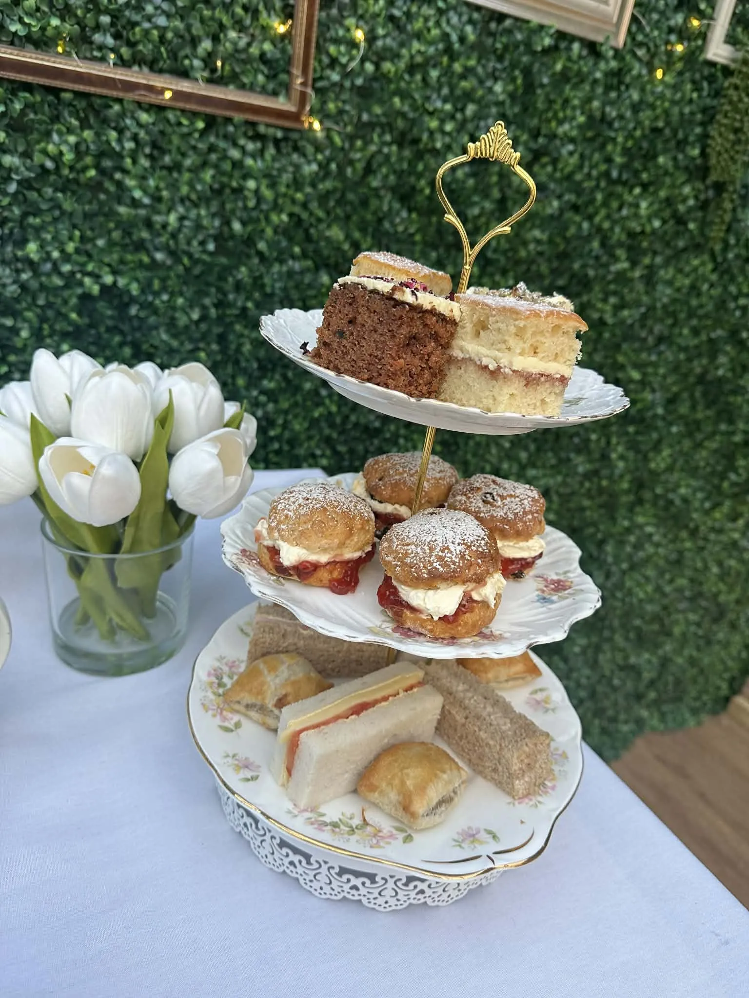 A three tier afternoon tea stand with cakes, scones and finger sandwiches