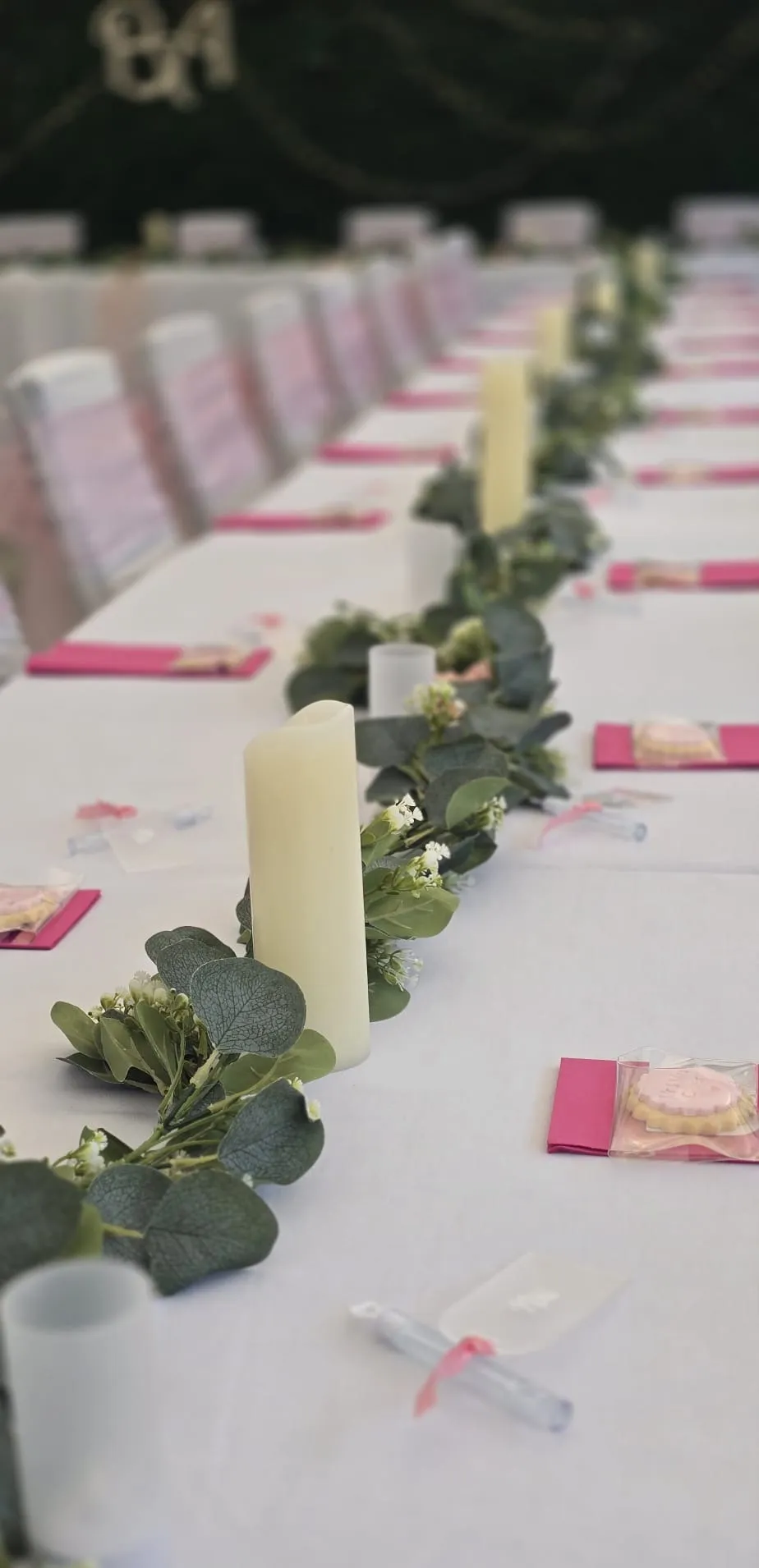 A long white table with pink napkins, candles and a eucalyptus garland