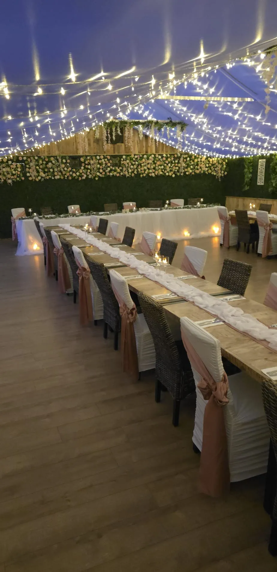 The wedding space at dusk with long tables, candlelight and a canopy of fairy lights
