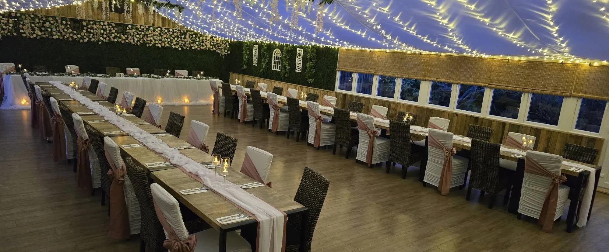 The marquee end dressed for a wedding, long tables beneath a canopy of fairy lights