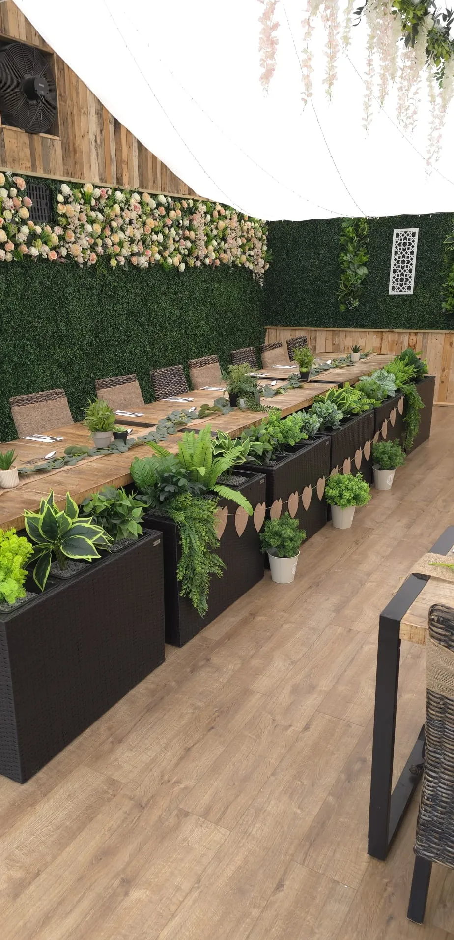 A rustic table laid with runners and greenery beside planter boxes