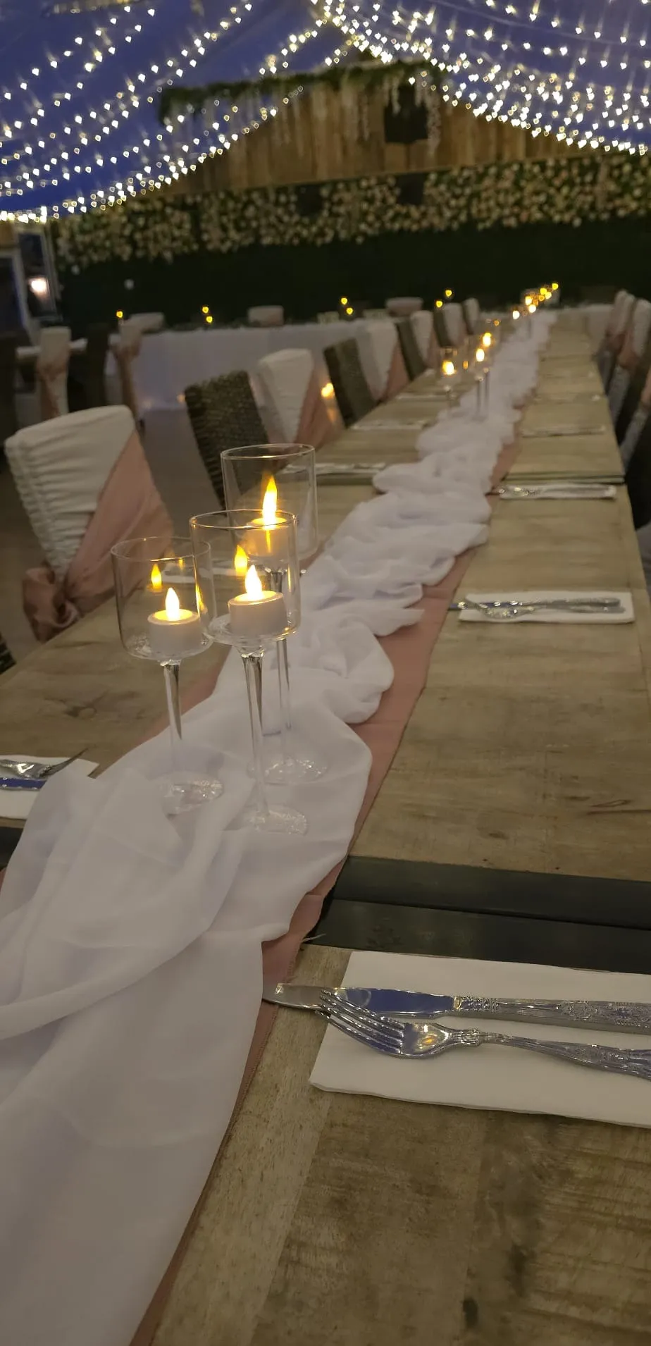A long wedding table by candlelight with a chiffon runner and place settings