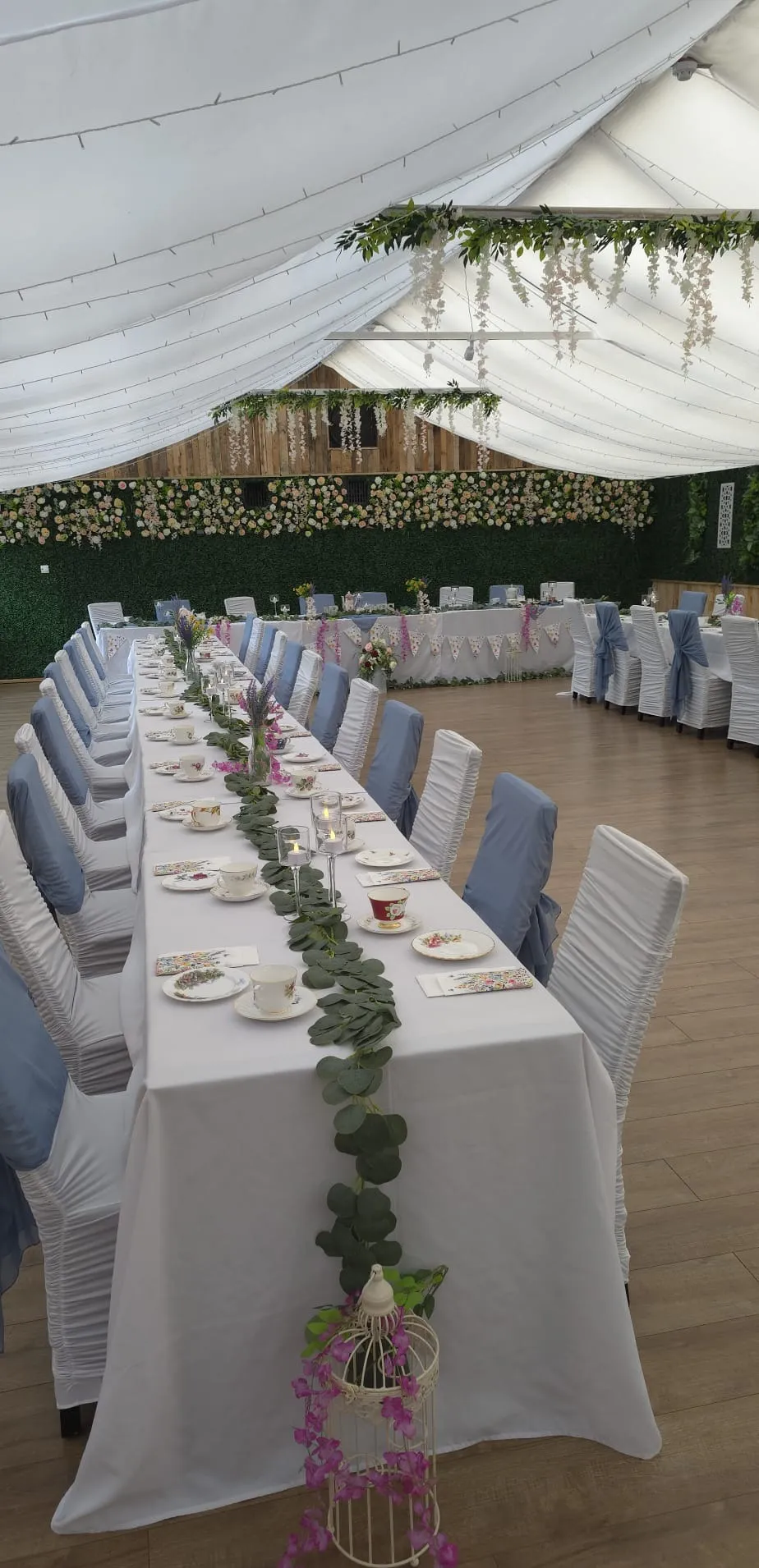 A tea party table with a birdcage, candles and wisteria overhead
