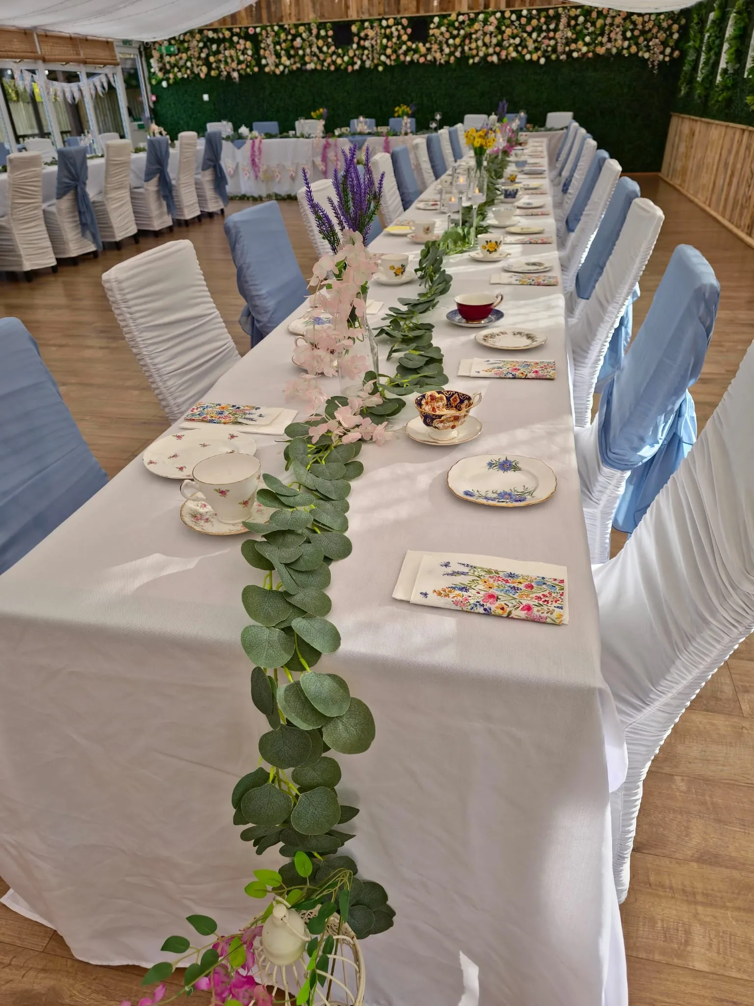 A long table with vintage china, wildflower napkins and a eucalyptus garland